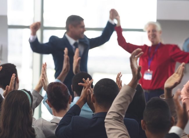 Rear view of diverse business people applauding and celebrating while they are sitting in front of mixes race and Caucasian business executives at business seminar in office building