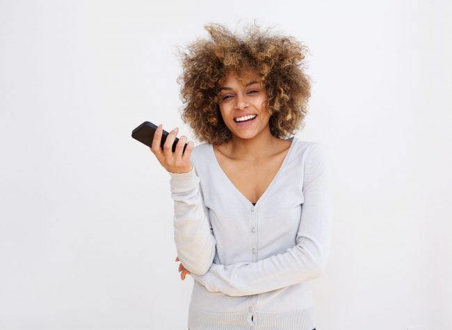 Portrait of happy young black woman with cellphone against white background